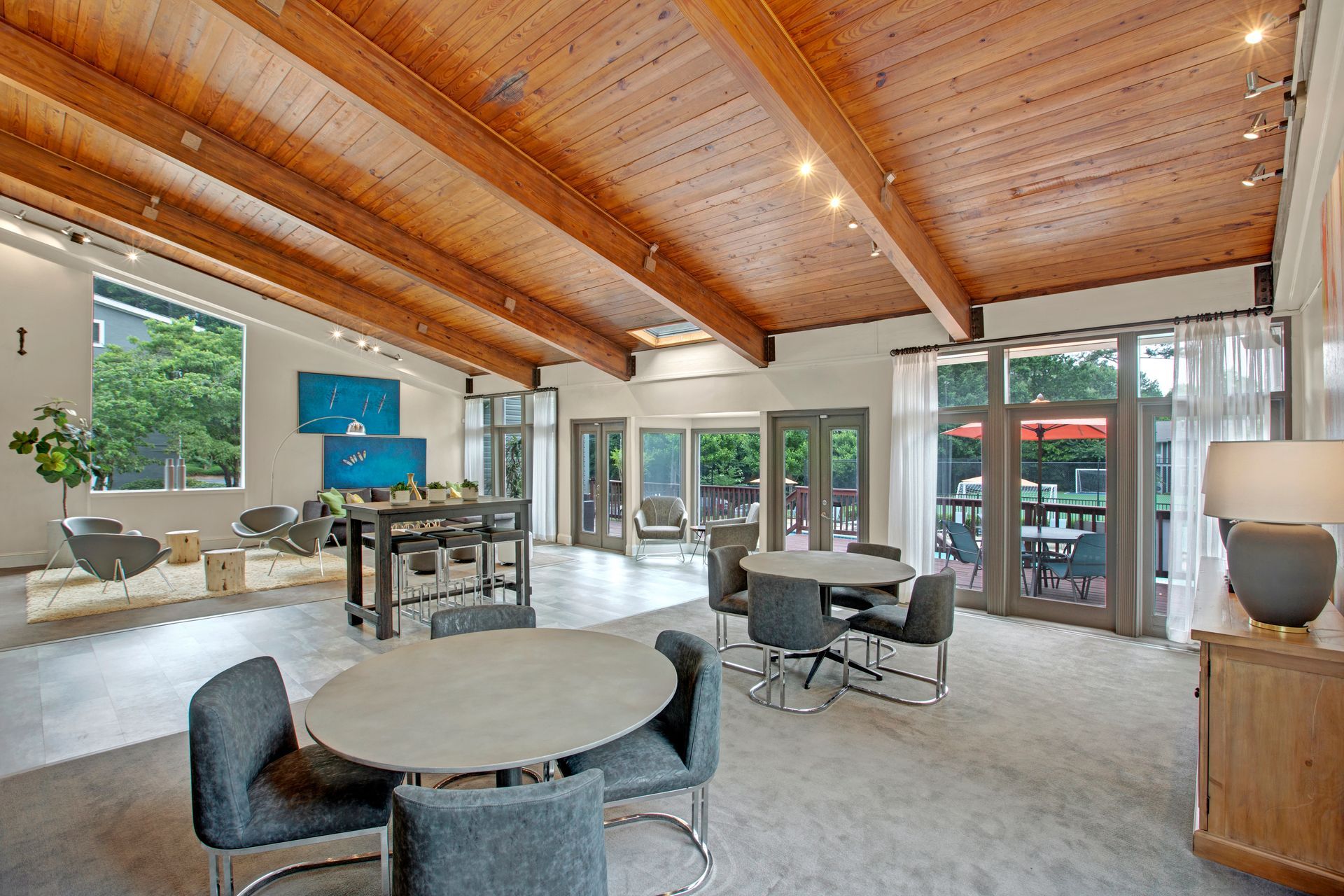 Modern open-plan living room with wood-beamed ceiling, gray furniture, and large windows