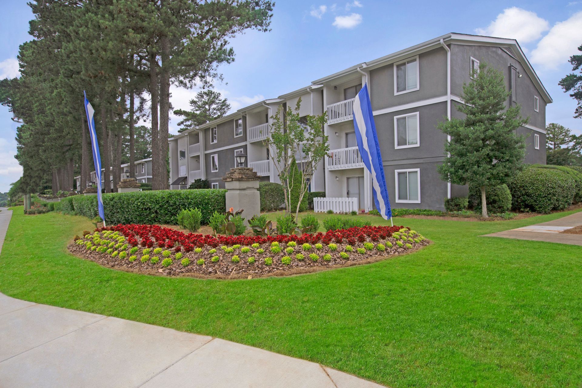 Apartment building with blue banners and a red flower bed along a green lawn and sidewalk