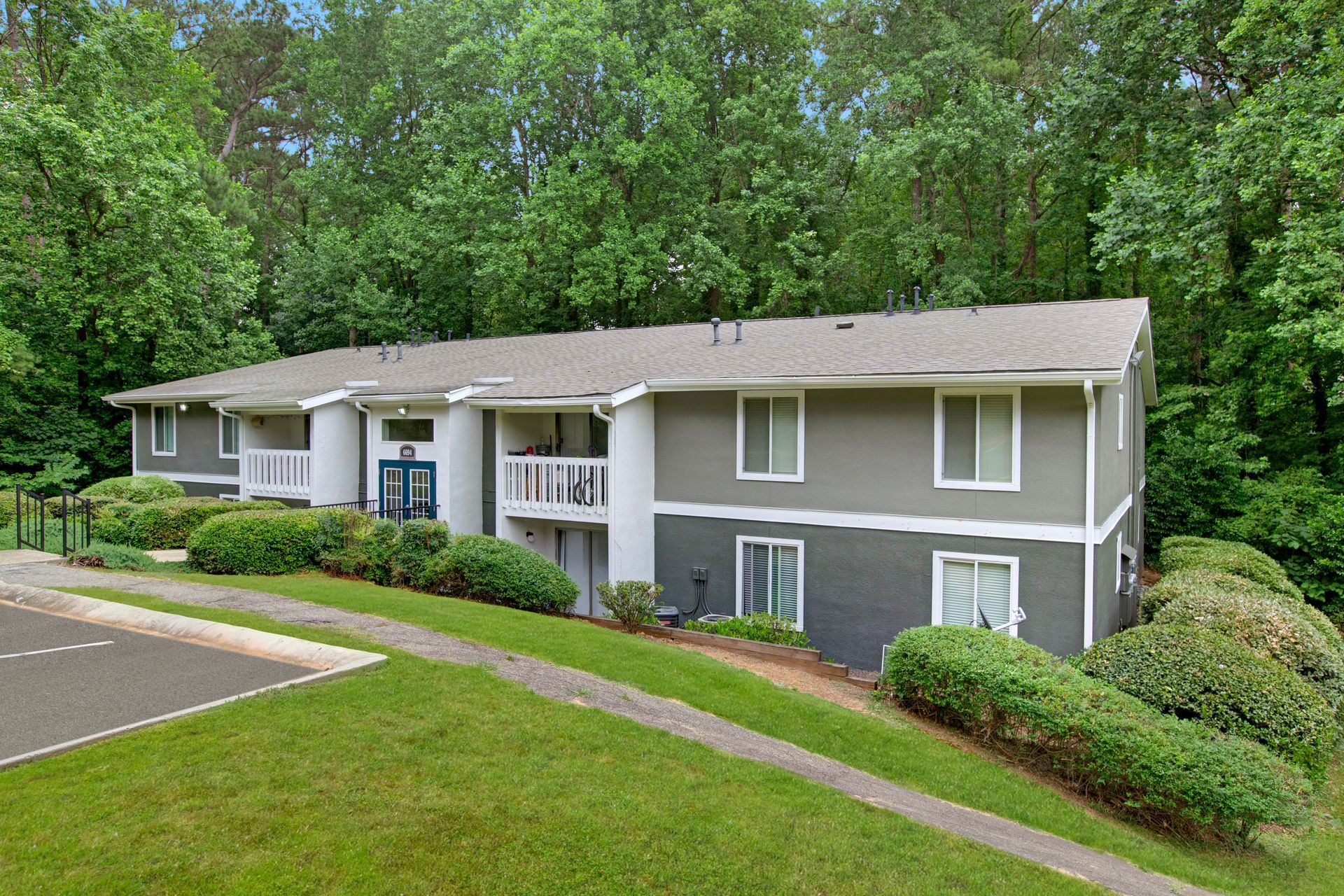 Suburban apartment building with gray siding and white trim, surrounded by trees and landscaped grass.