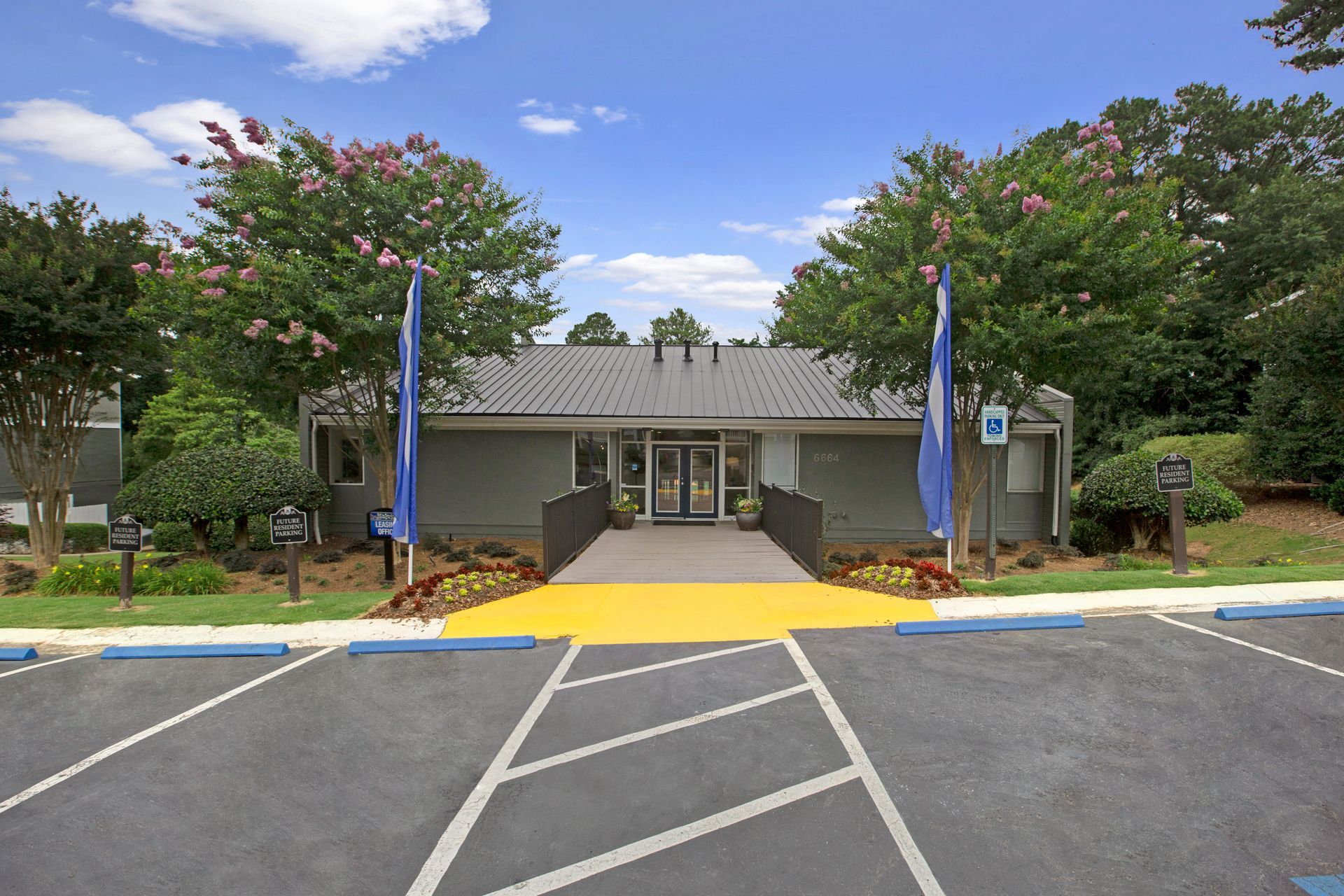 Accessible building entrance with ramp, blue flags, and parking lot under a blue sky