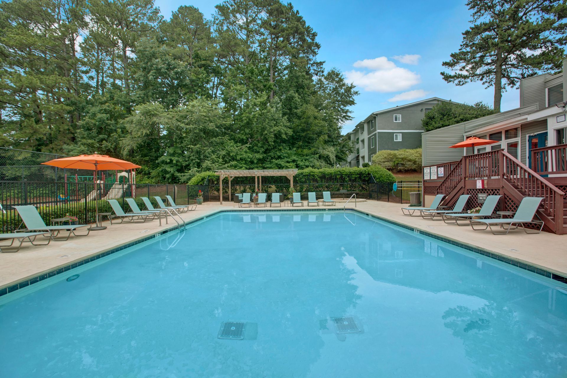 Outdoor swimming pool with lounge chairs, orange umbrella, and apartment buildings in the background