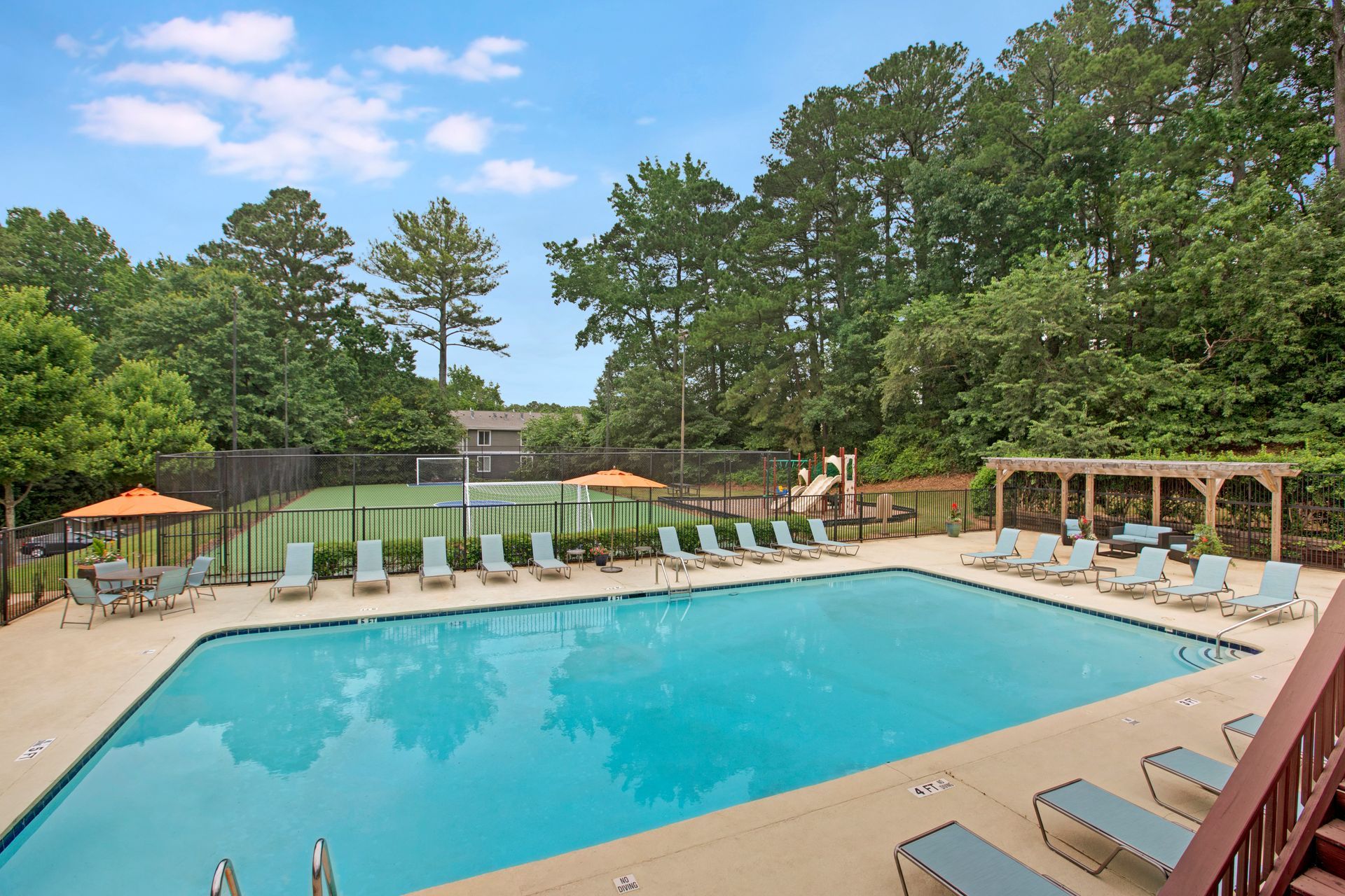 Outdoor swimming pool with lounge chairs, umbrellas, and trees under a clear blue sky