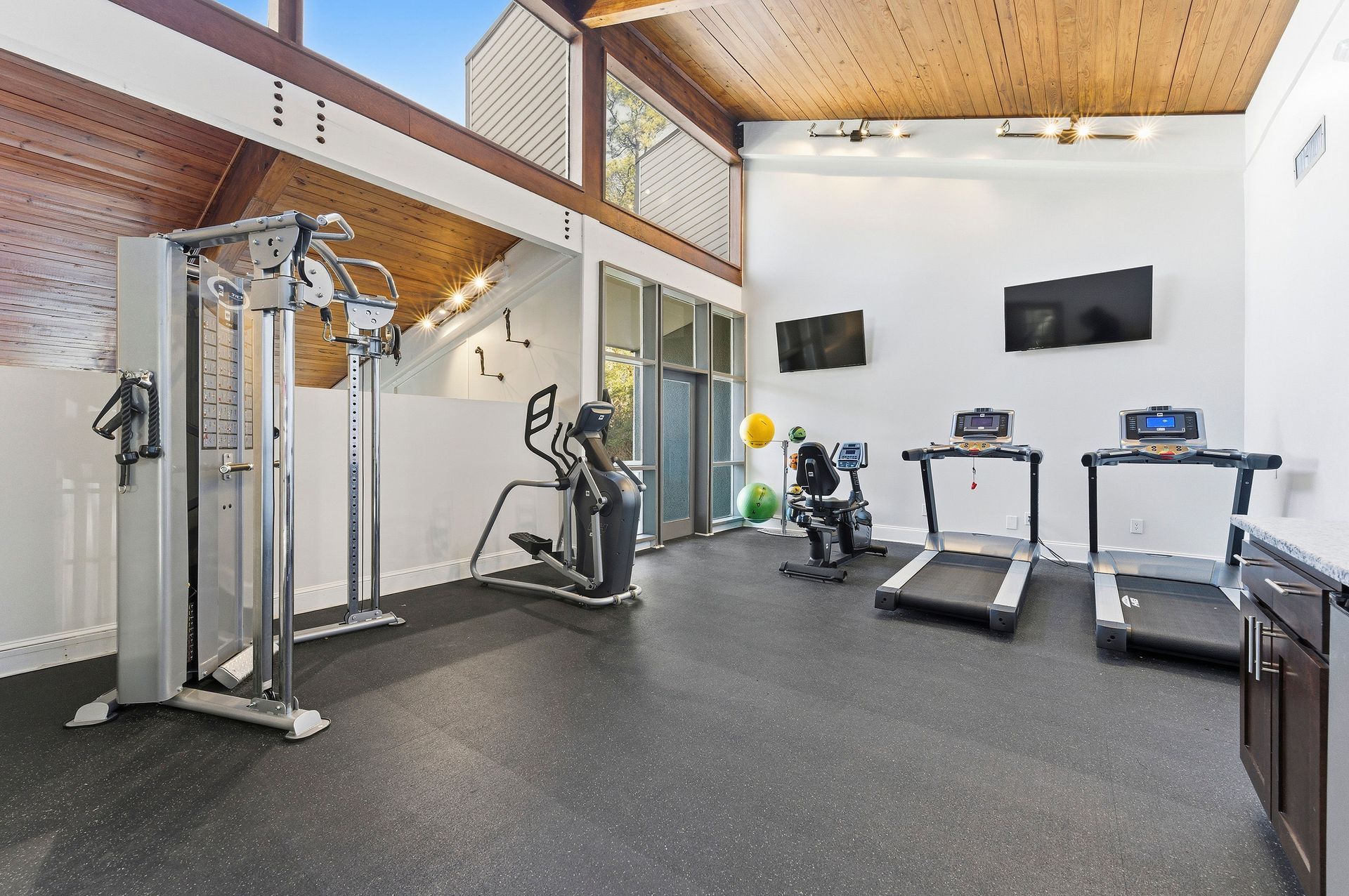 Modern gym room with cable machine, treadmill, elliptical, and wall-mounted TVs