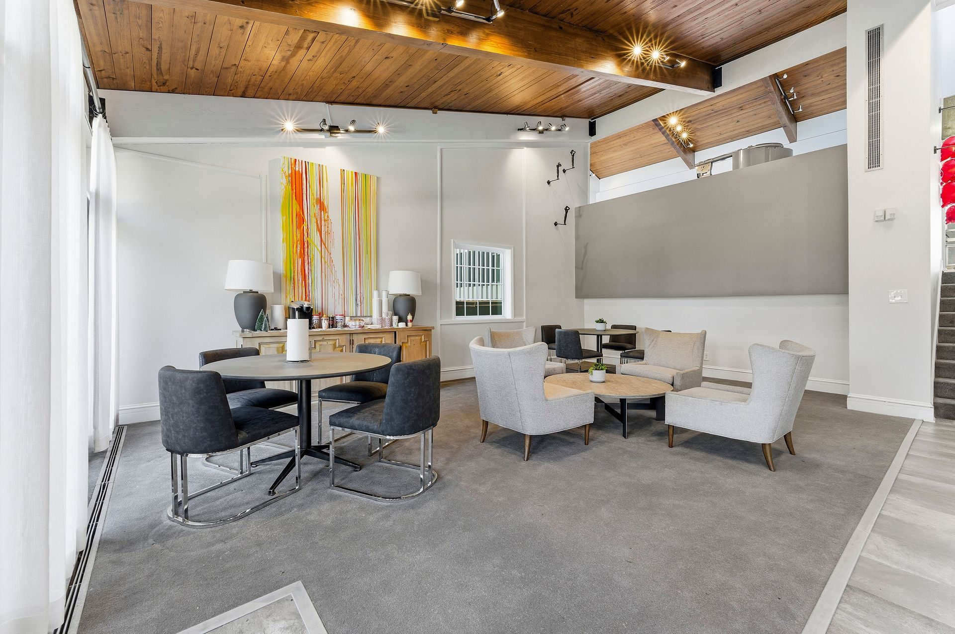 Modern dining room with gray chairs, wooden table, colorful wall art, and exposed wood ceiling