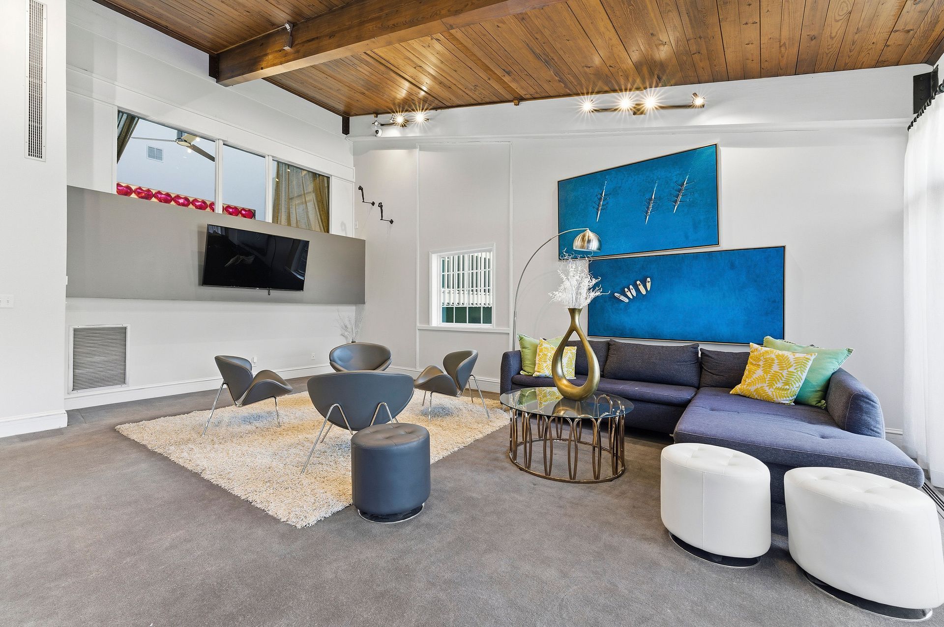 Modern living room with gray sofa, blue wall art, coffee table, and exposed wood ceiling