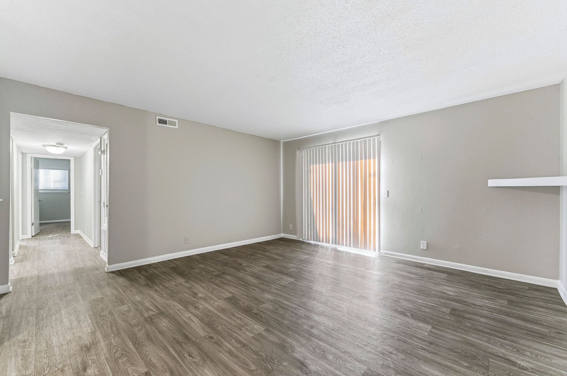 Empty living room with gray walls, wood-look floors, and vertical blinds on the sliding door.