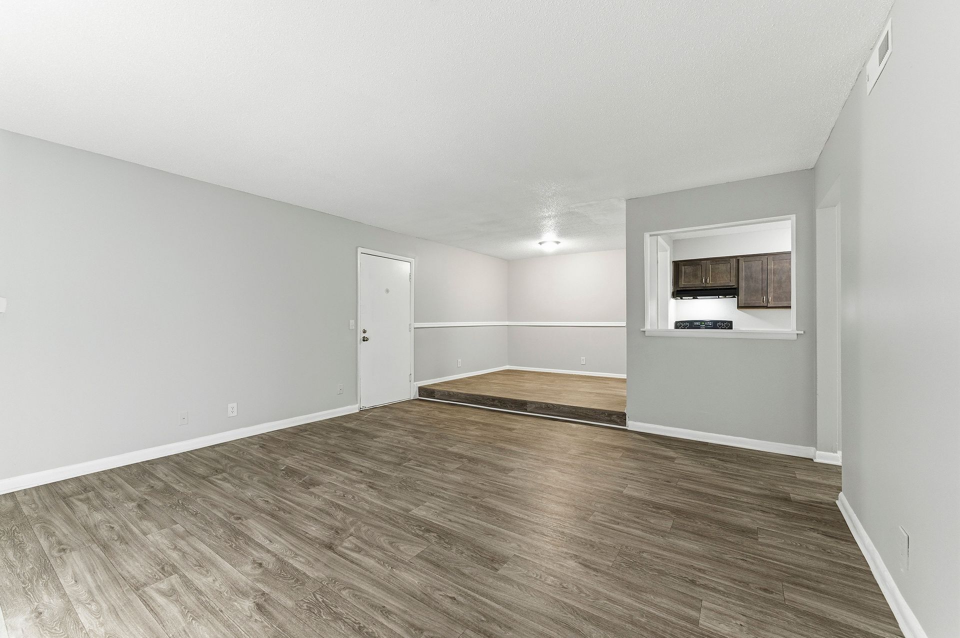 Empty gray living room with wood-look floor and pass-through opening to a kitchen area