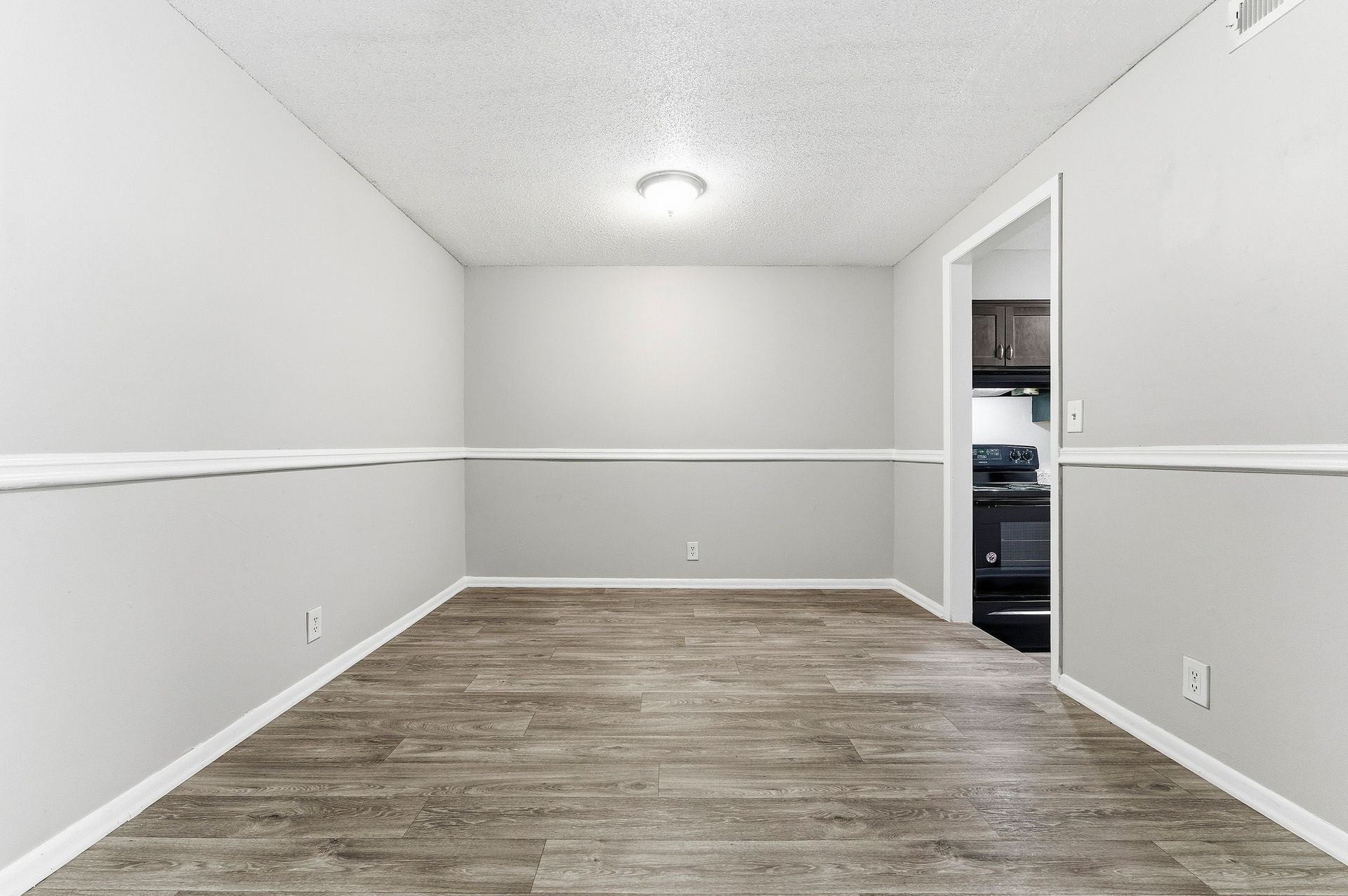 Empty gray room with wood-look floor, white trim, and an open doorway to a closet or utility area