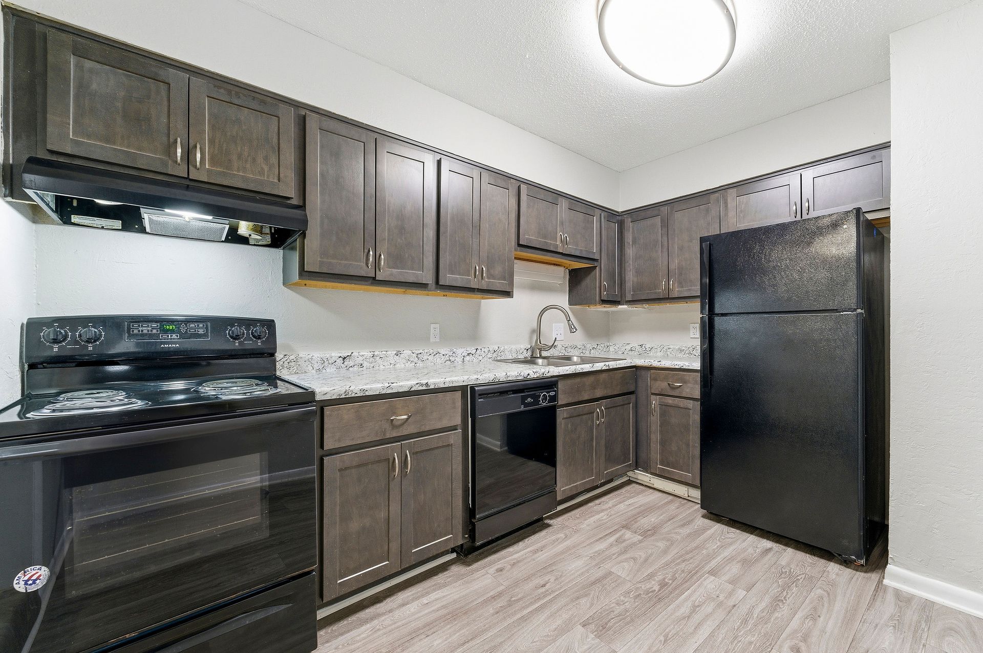 Modern kitchen with dark cabinets, black appliances, and light wood flooring