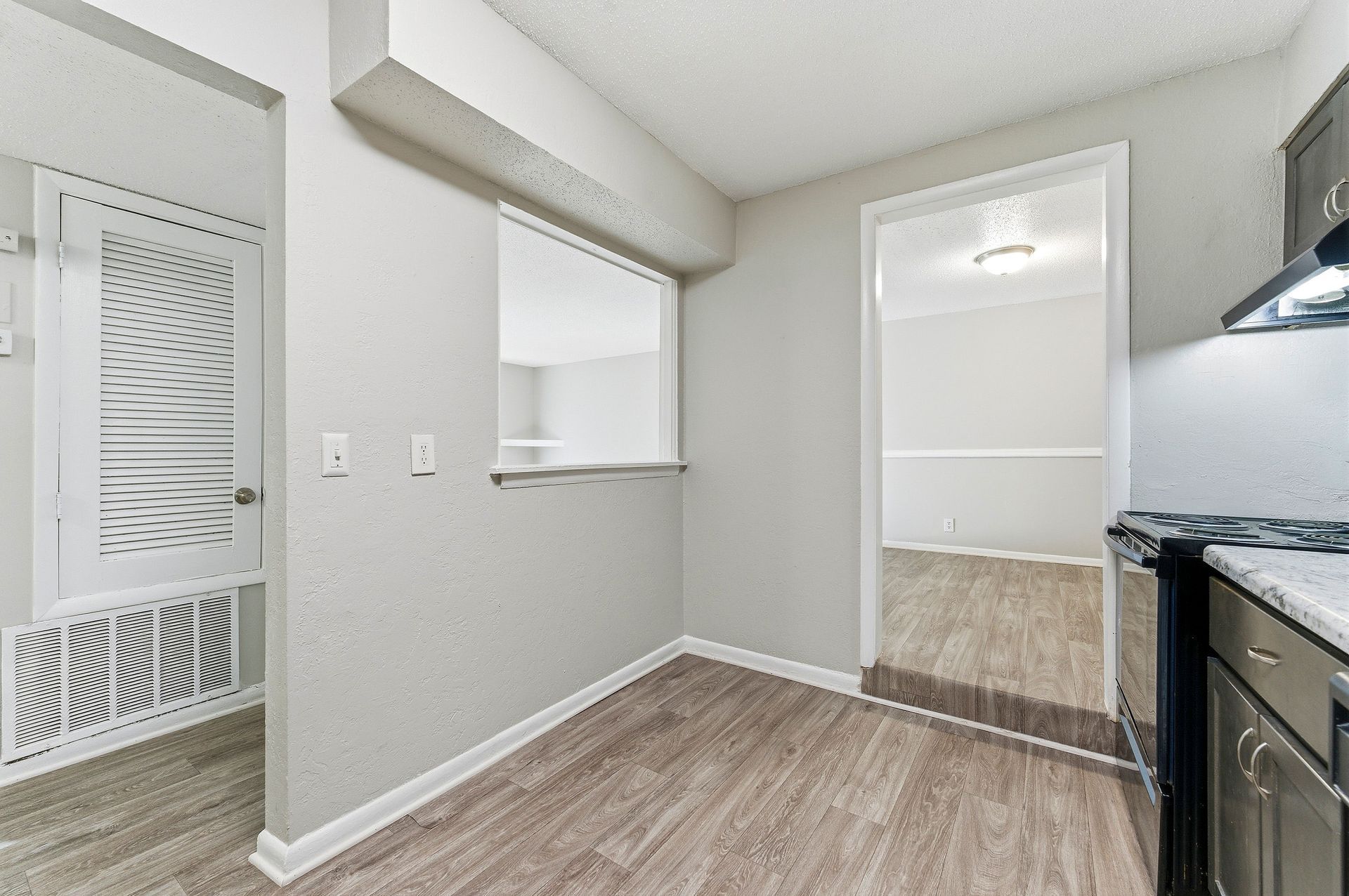 Empty kitchen with gray walls, wood-look floor, pass-through window, and black stove on the right