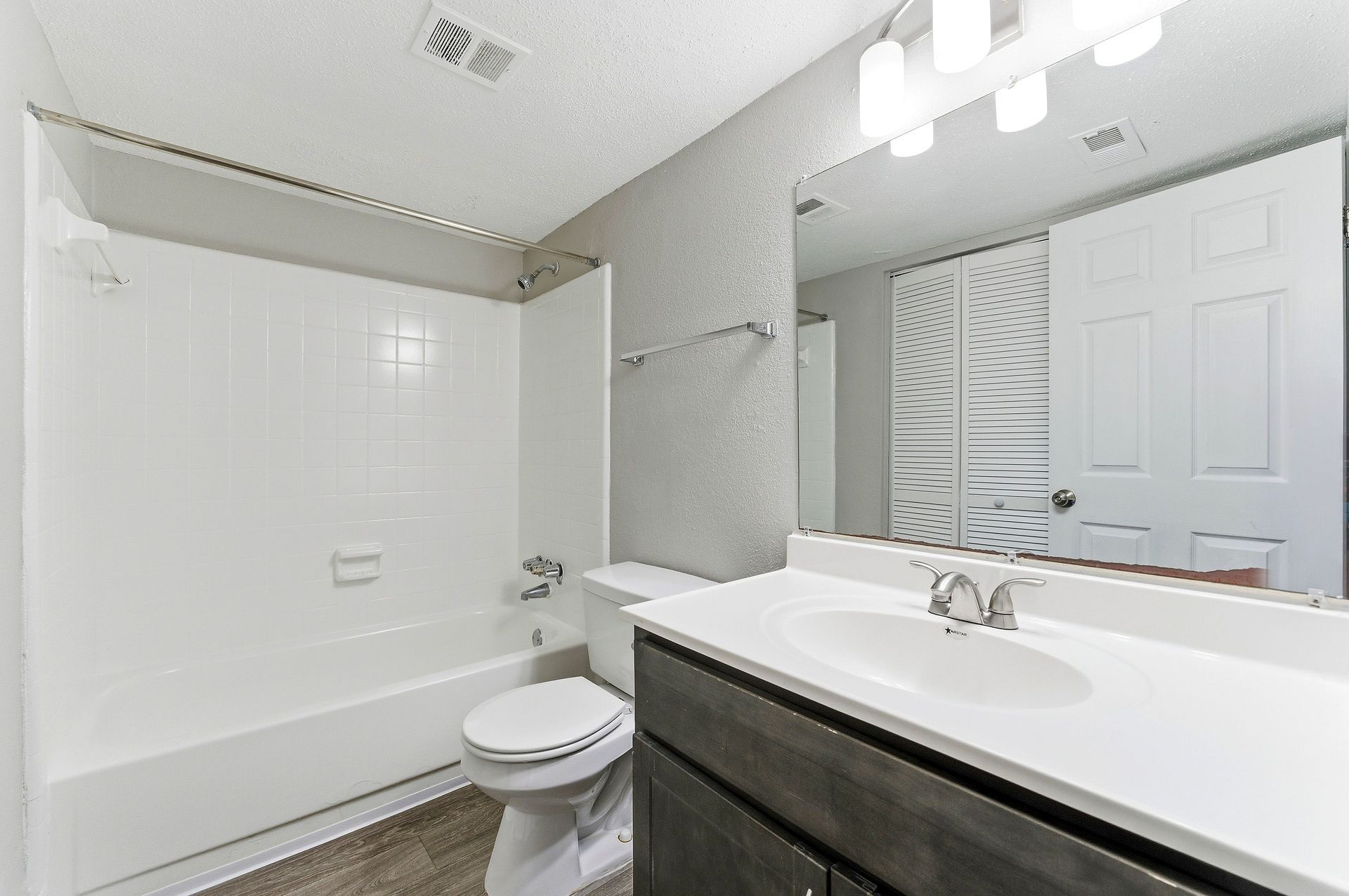 Bright white bathroom with tub, toilet, and dark vanity with mirror and sink