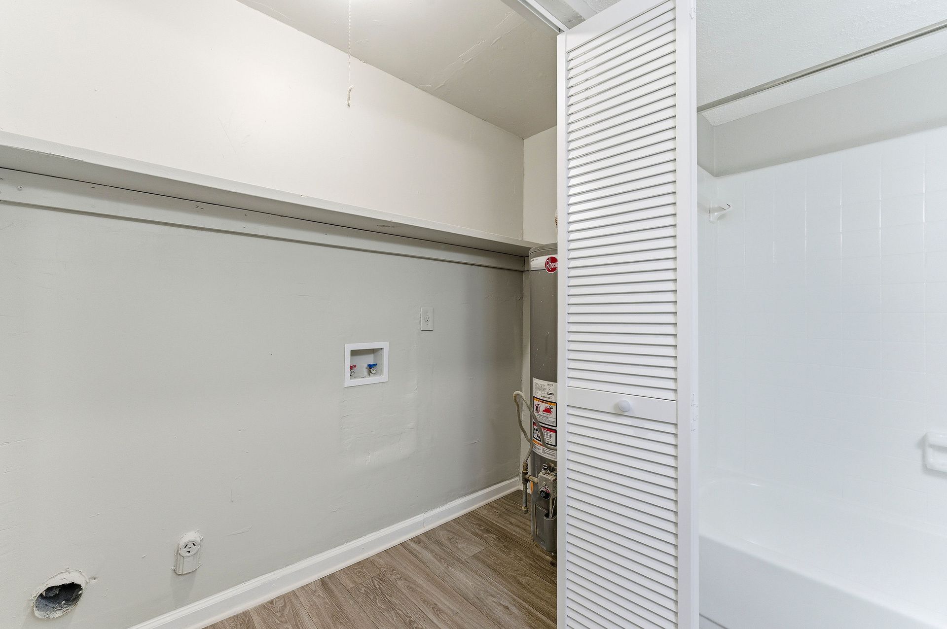 Empty white laundry room with washer/dryer hookups, shelf, and louvered closet door