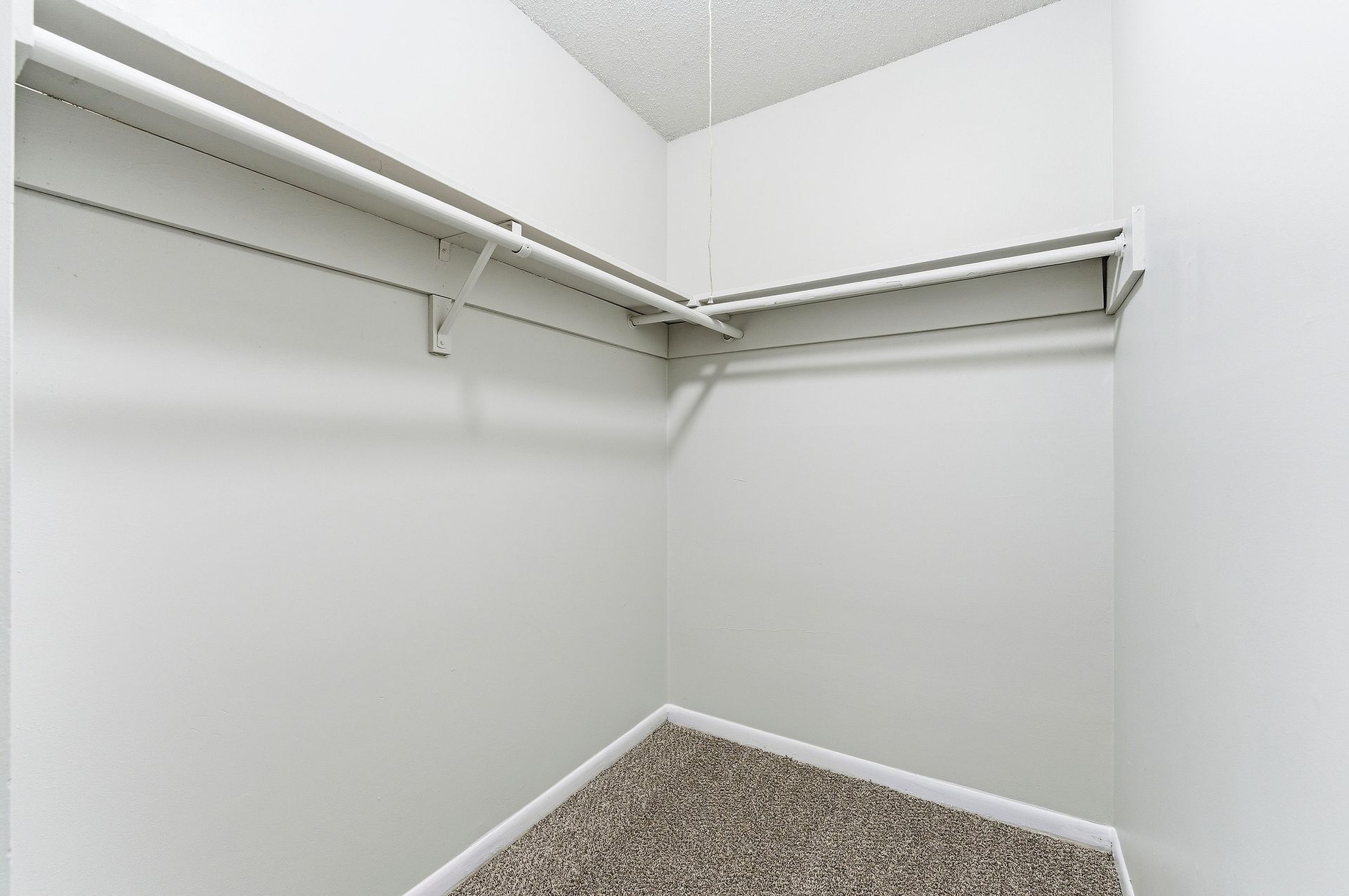 Empty walk-in closet with white walls, wire shelving, and carpeted floor
