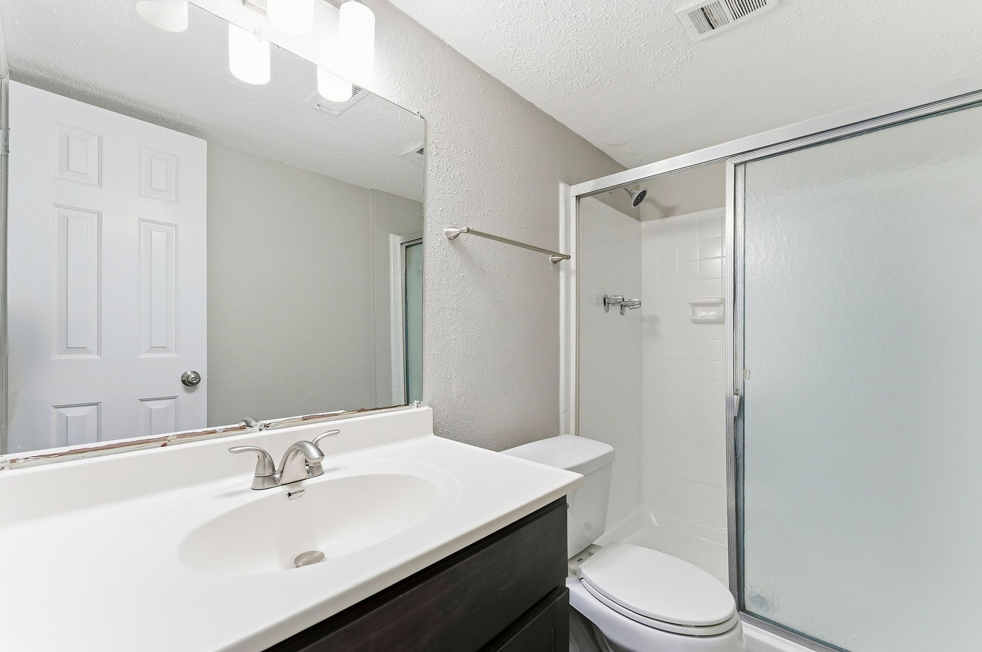 Bright bathroom with white vanity, sink, mirror, toilet, and frosted glass shower door.