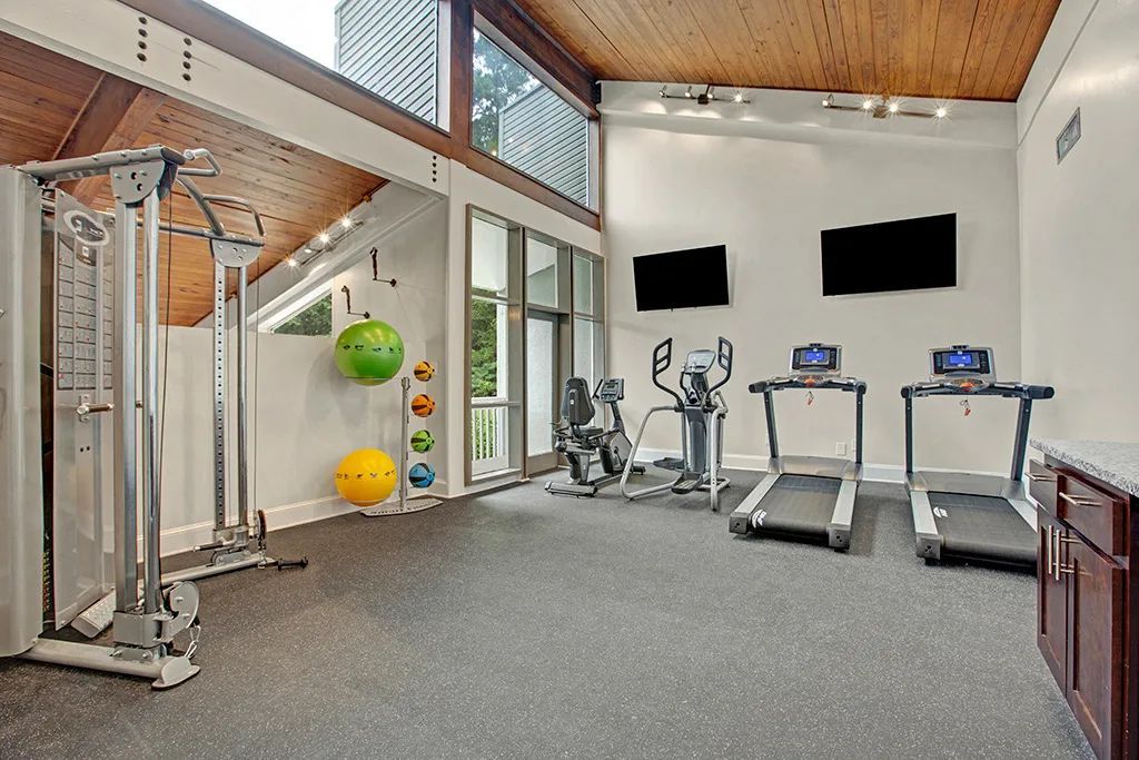 Modern gym with treadmills, exercise bikes, cable machine, and large wall-mounted TVs