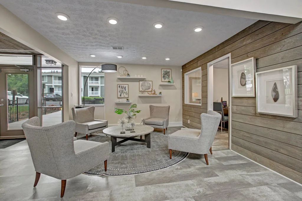 Modern living room with gray chairs, glass coffee table, and neutral decor in soft lighting