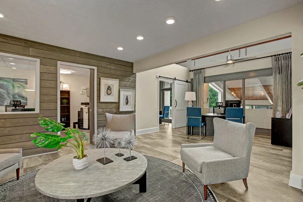 Bright modern living room with gray chairs, round coffee table, and open dining area leading to a kitchen