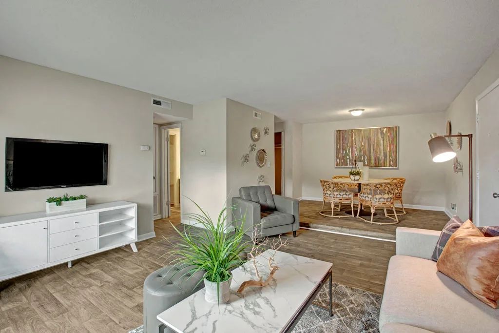 Bright living and dining room with white furniture, wall-mounted TV, and neutral decor