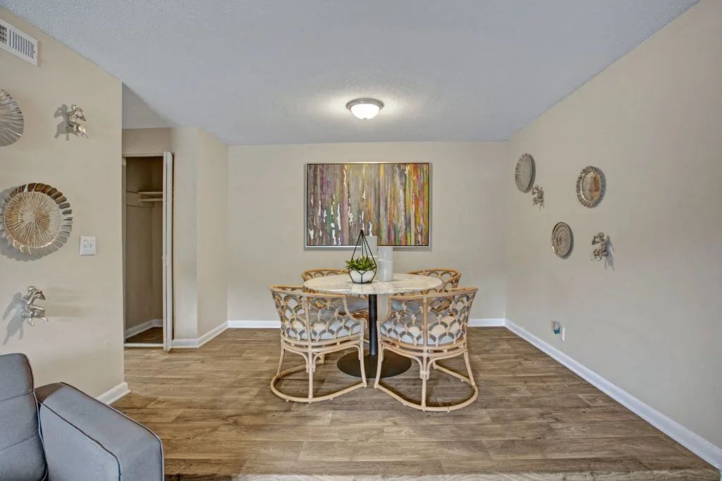Bright dining room with wicker table and chairs, neutral walls, wood flooring, and wall art.