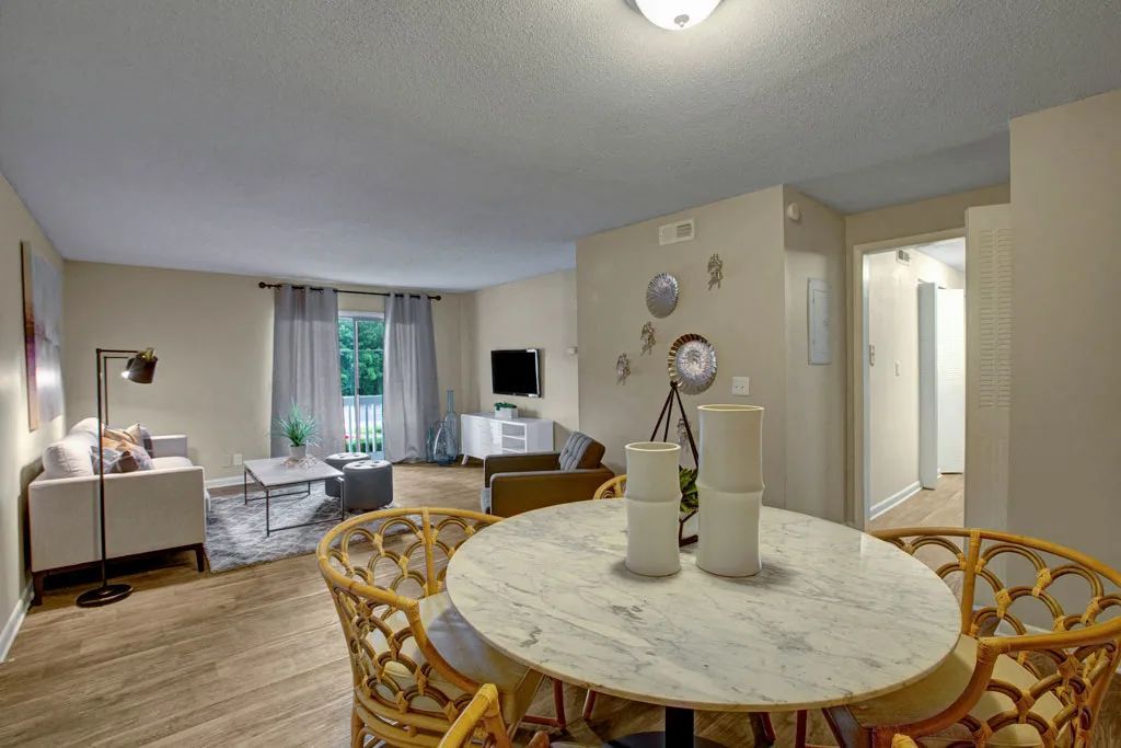 Bright living-dining room with wicker chairs, round table, sofa, TV, and sliding glass doors.