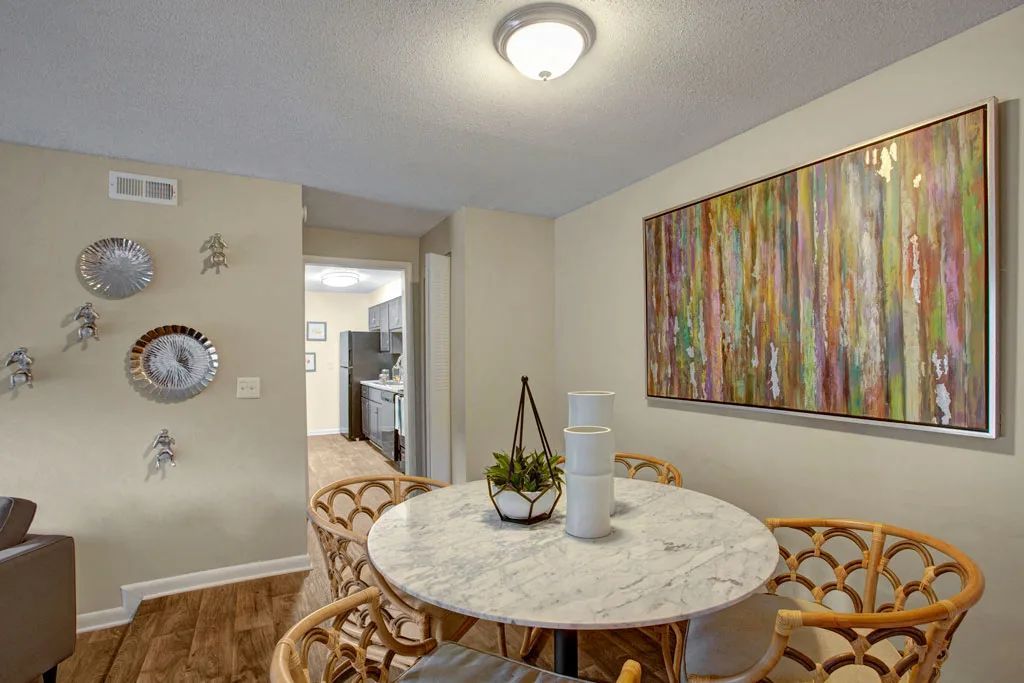 Dining nook with round marble table, wicker chairs, and colorful wall art in a beige room