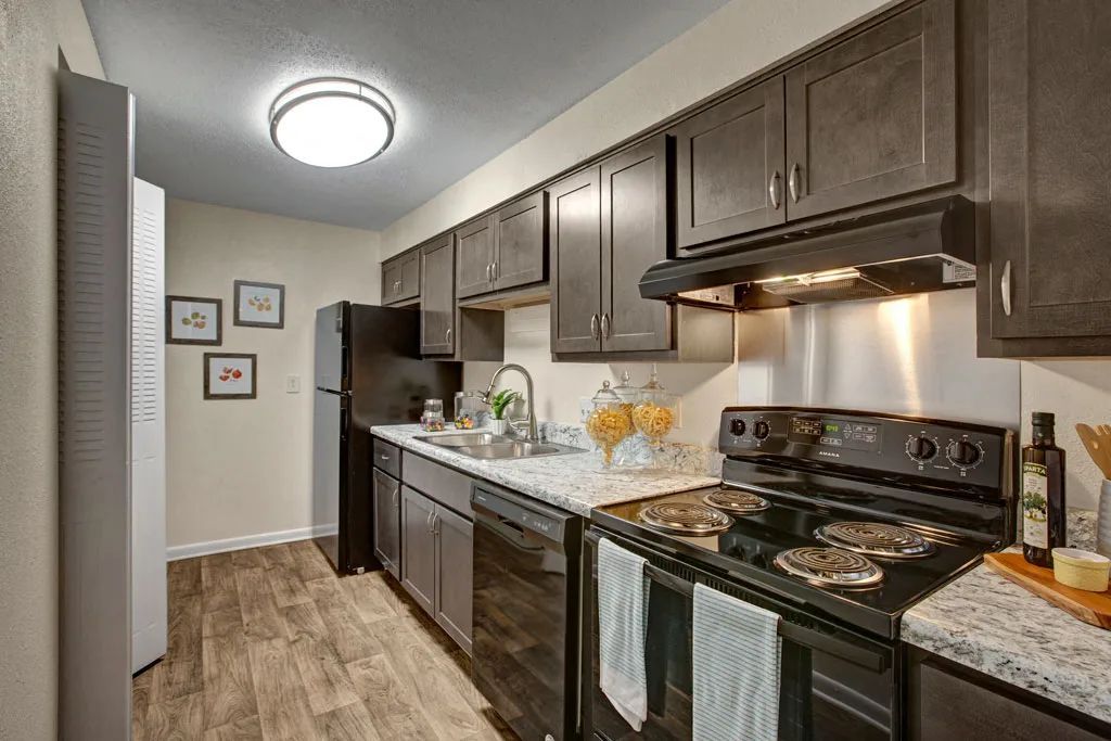 Modern kitchen with dark cabinets, granite counters, black stove, and tiled floor along a narrow hallway