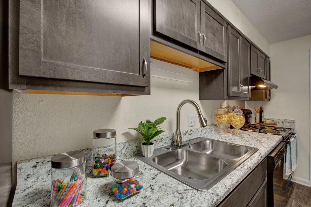 Modern kitchen countertop with sink, dark cabinets, granite counter, and colorful candy jars