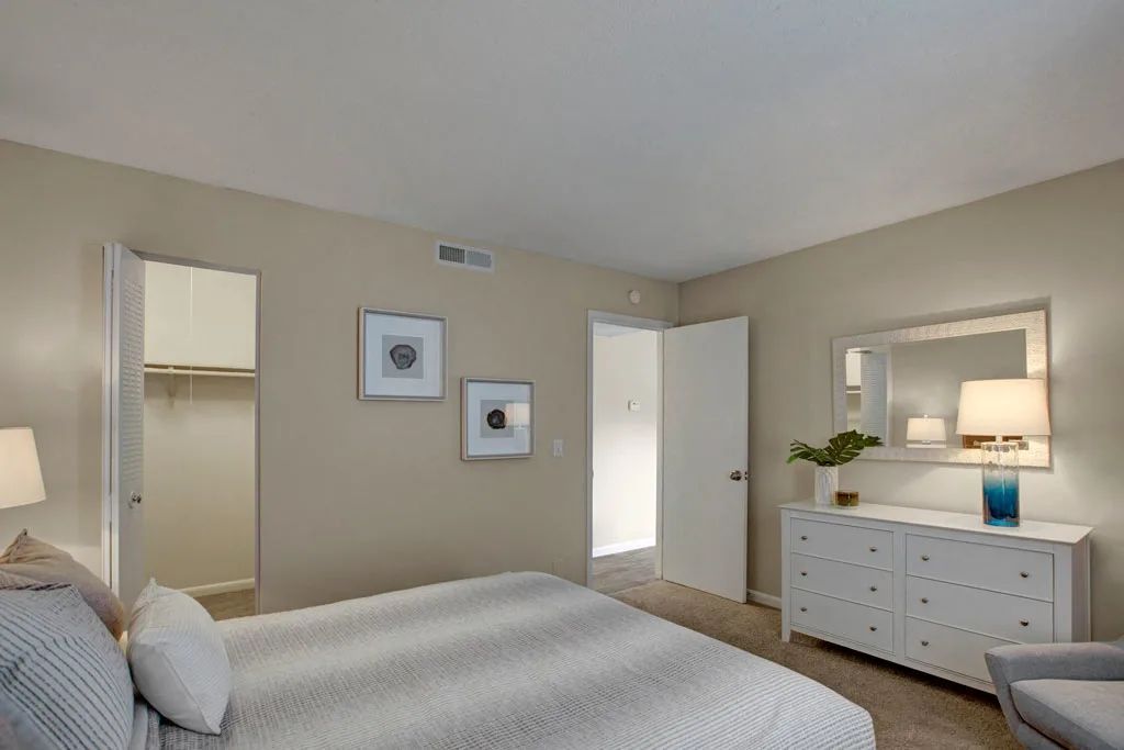 Bright bedroom with a bed, dresser, mirror, and soft beige walls