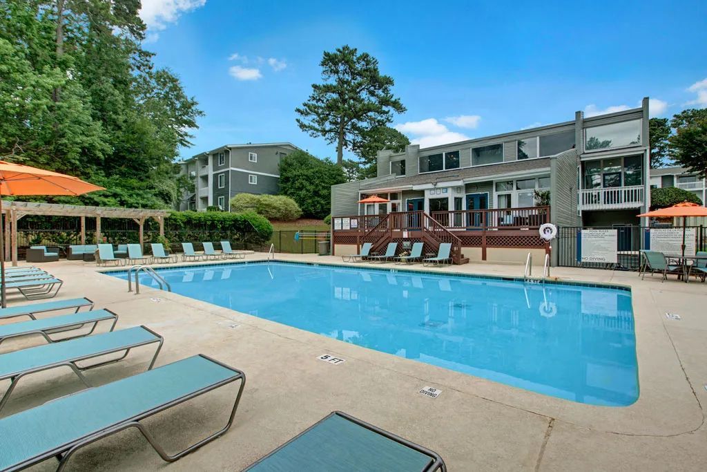 Outdoor swimming pool with lounge chairs, umbrellas, and apartment buildings in the background