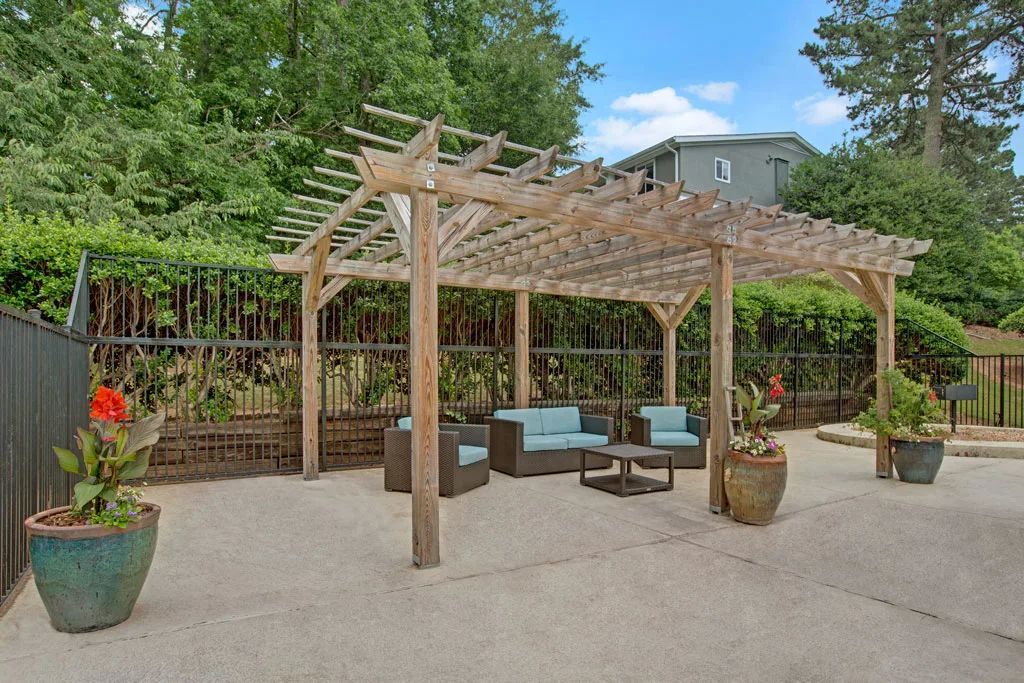 Backyard pergola with wicker seating, potted plants, and a patio surrounded by trees