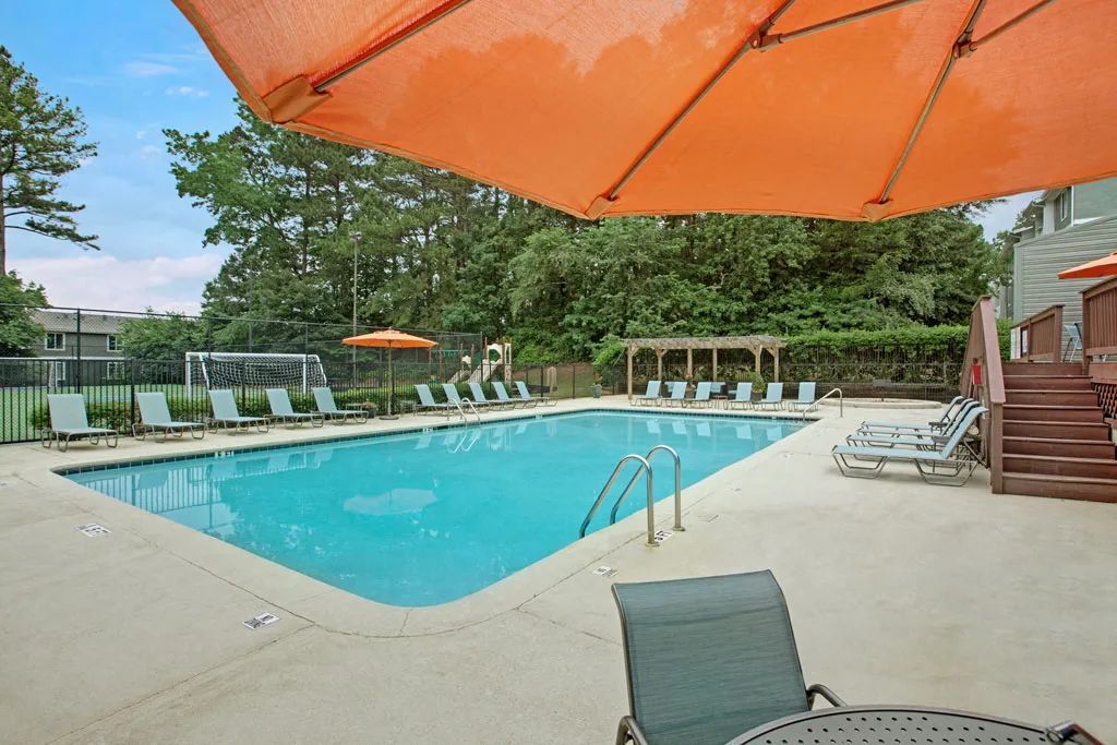 Outdoor swimming pool with orange umbrellas, lounge chairs, and a poolside deck surrounded by trees.