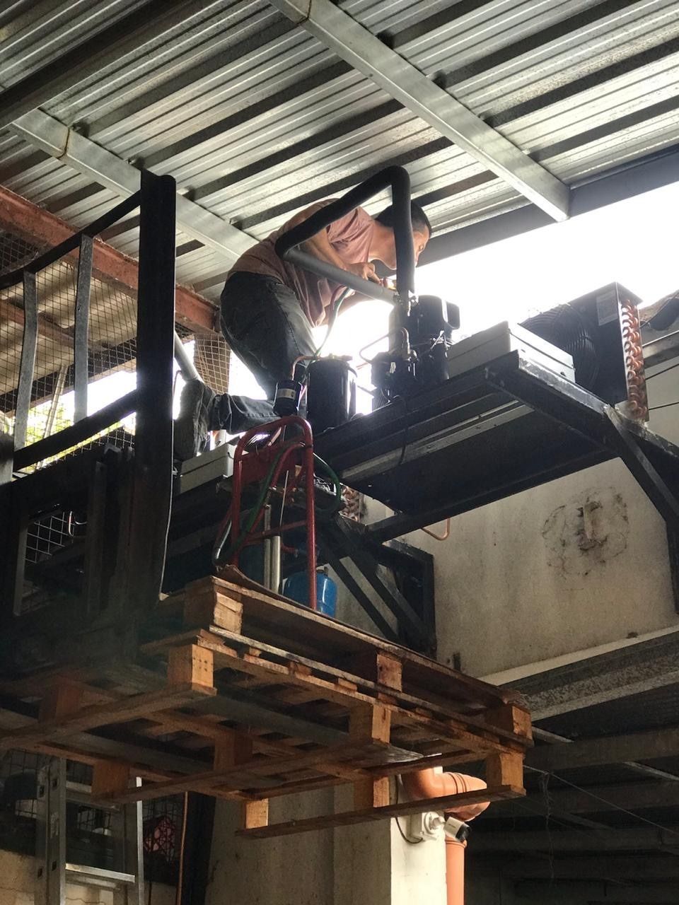 Una persona arrodillada sobre una paleta de madera levantada por una carretilla elevadora, trabajando en una estructura