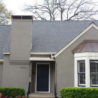 A gray house with a blue door and a chimney on the roof.