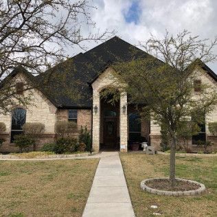 A large brick house with a black roof and a tree in front of it.