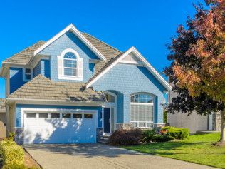 A blue house with a white garage door and a tree in front of it.
