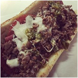 A close up of a steak sandwich with cheese, peppers, onions, and sauce on a bun