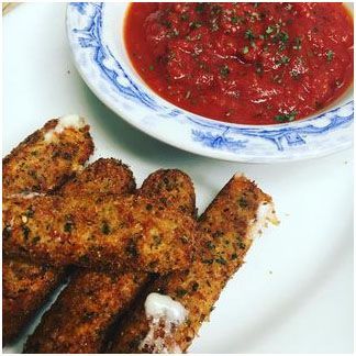 A plate of mozzarella sticks next to a bowl of tomato sauce