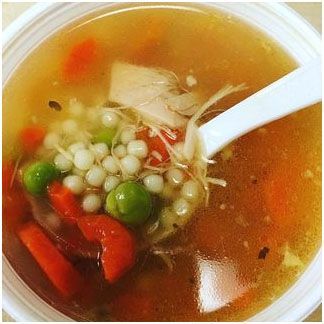 A bowl of chicken pastina soup and a spoon in it