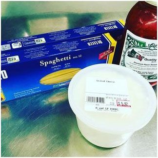 A box of spaghetti, a container of grated cheese, and a jar of tomato sauce sitting on a steel table