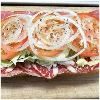 A sub sandwich with lettuce, tomatoes, onions and meat on a wooden cutting board