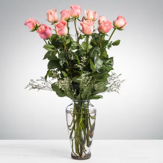 A bouquet of pink roses in a clear glass vase against a soft grey background.