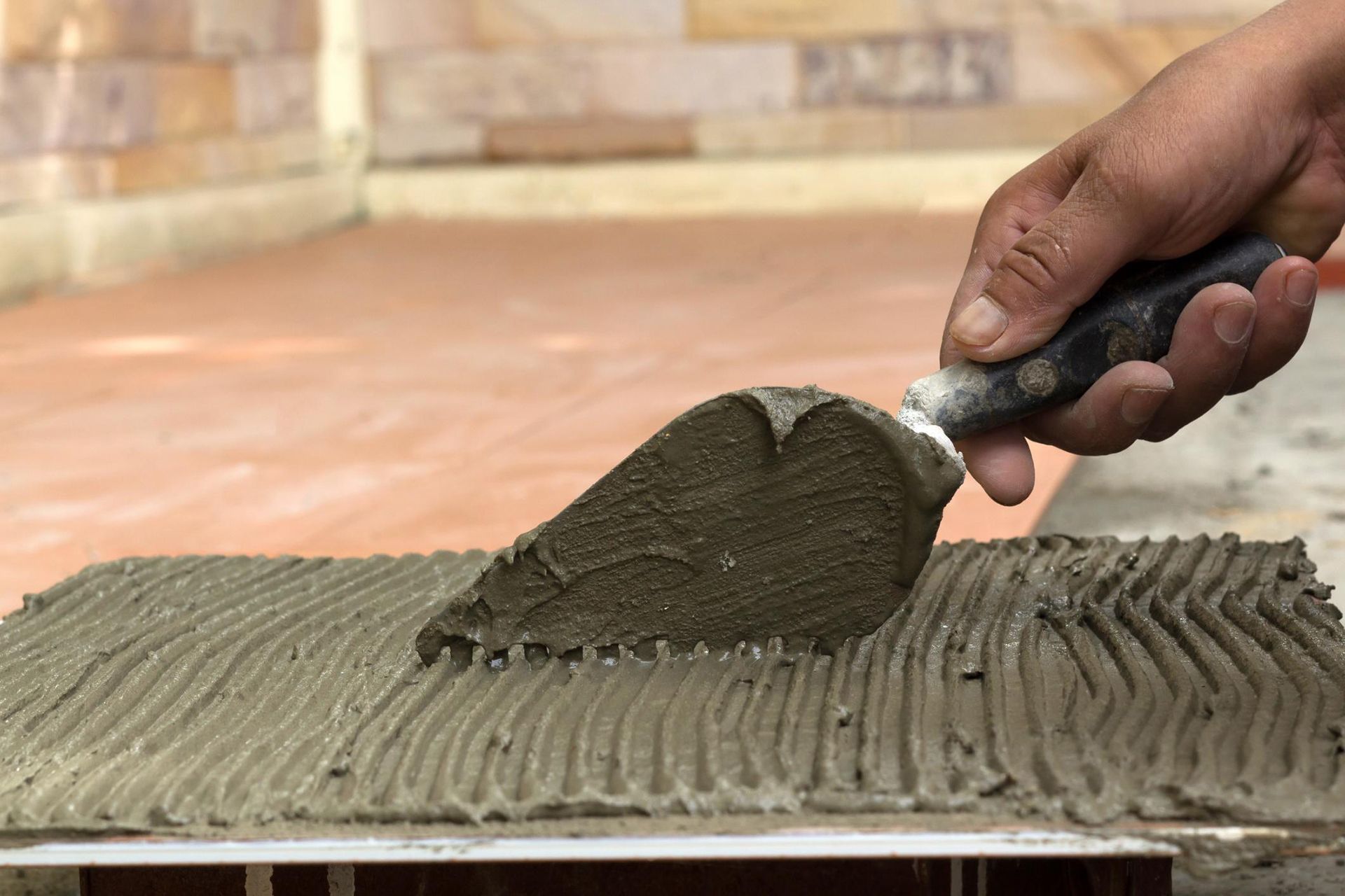 A person is spreading concrete on a tile with a trowel