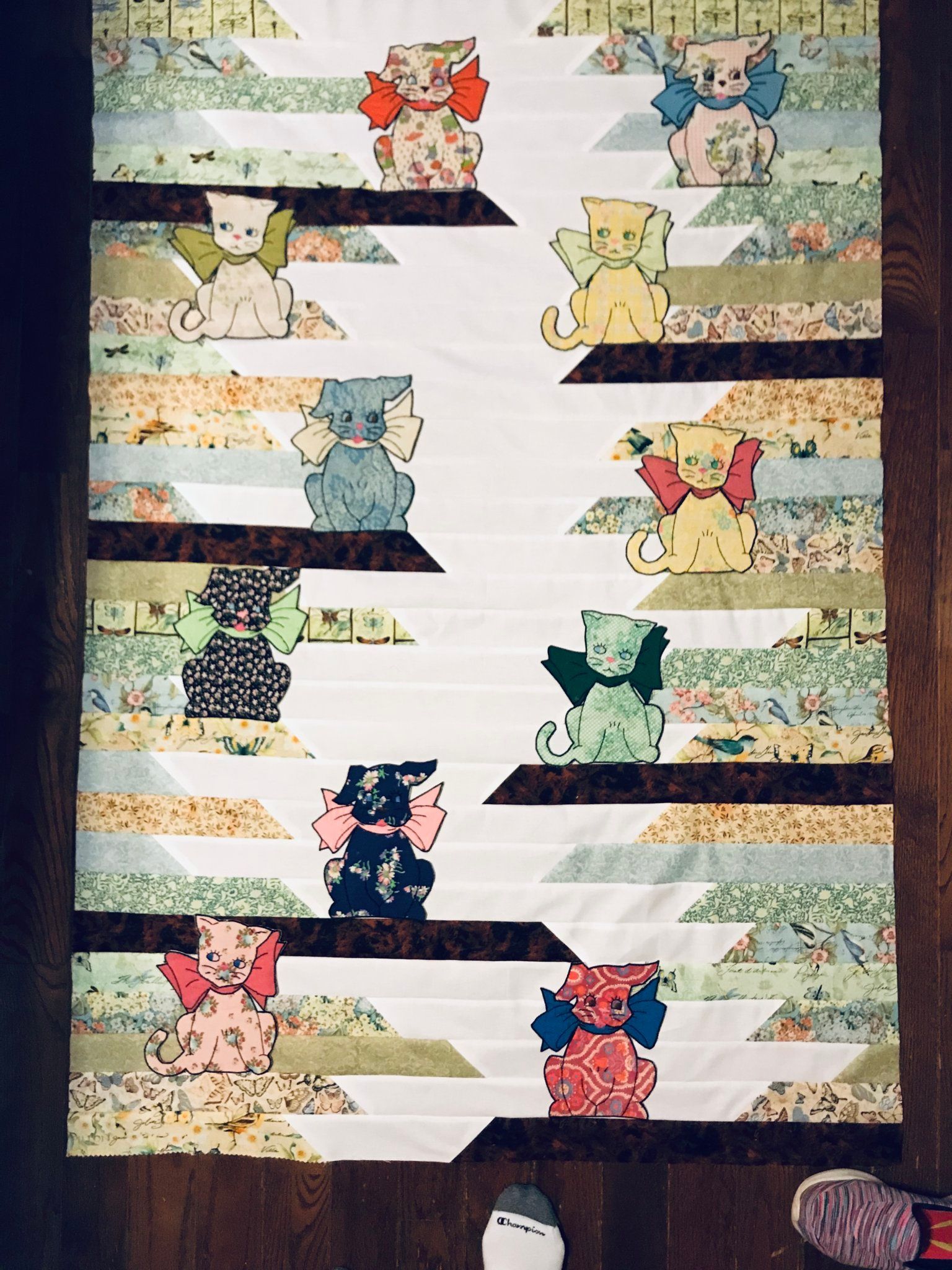 Quilt with colorful cat appliqués arranged in rows on striped fabric background