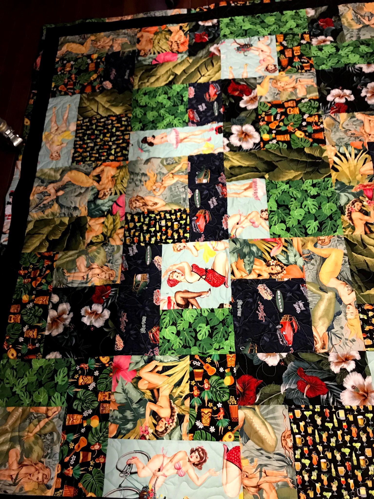 Patchwork quilt with floral and animal prints in black, green, orange, and white, spread flat on a bed.