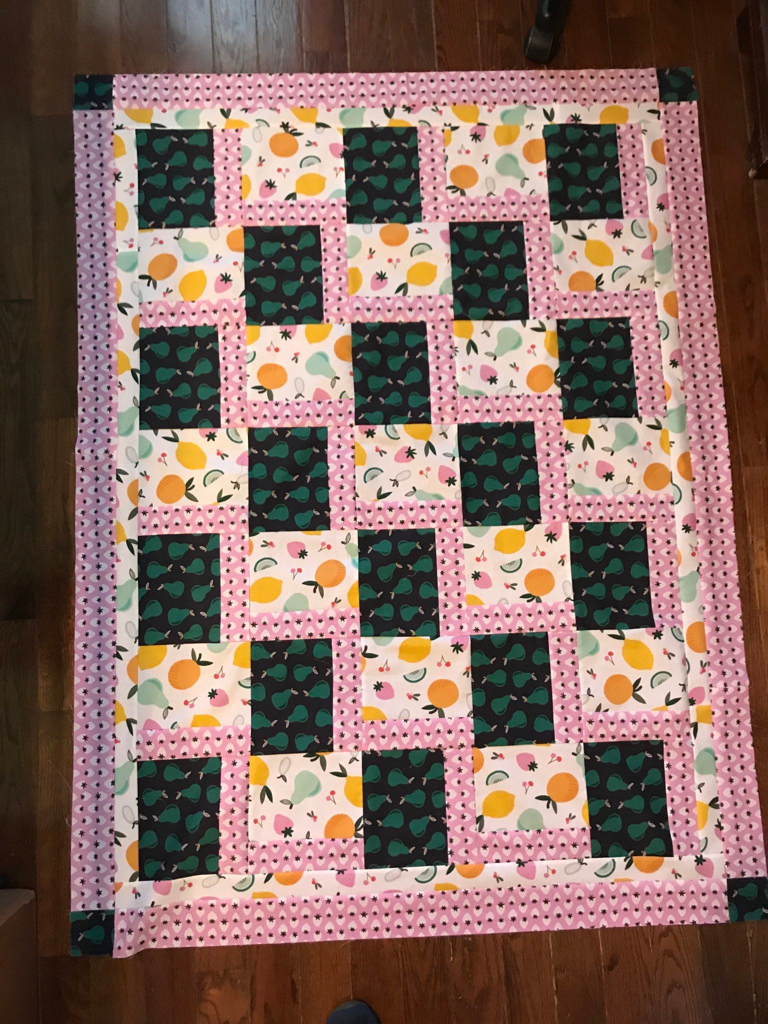 Pink quilt with green and floral patchwork squares arranged in a repeating grid pattern