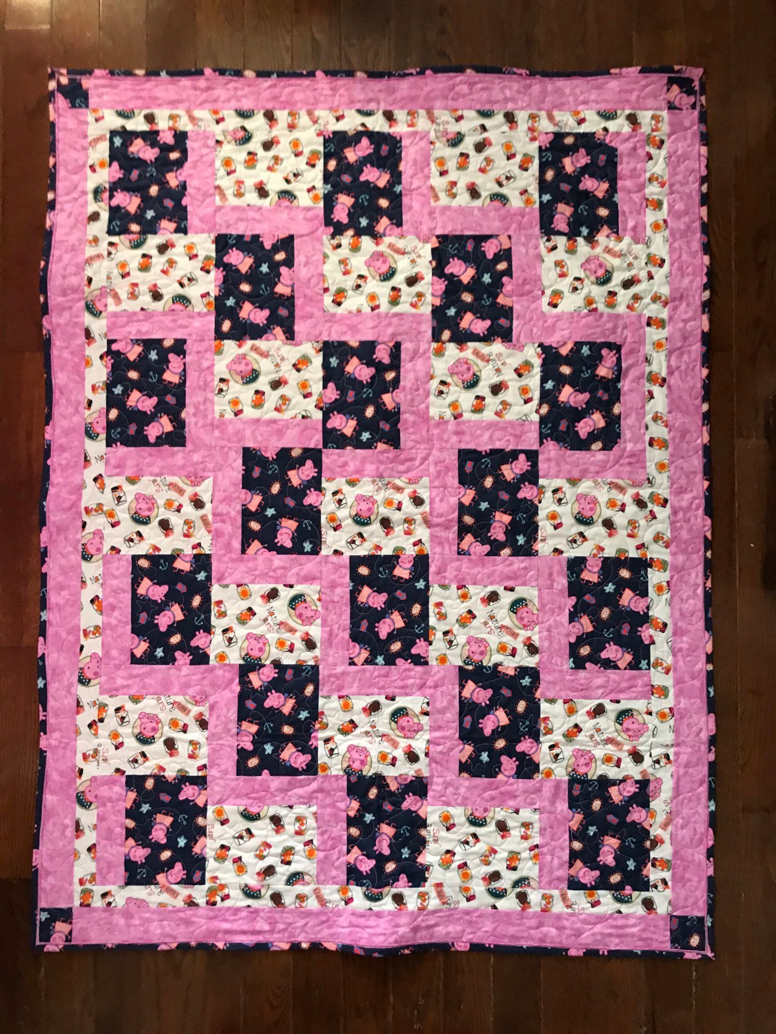 Pink and black patchwork quilt with floral prints on a wooden surface