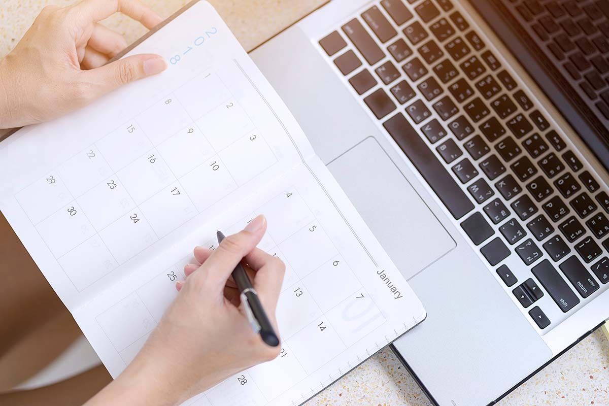 Person writing on calendar next to a laptop.
