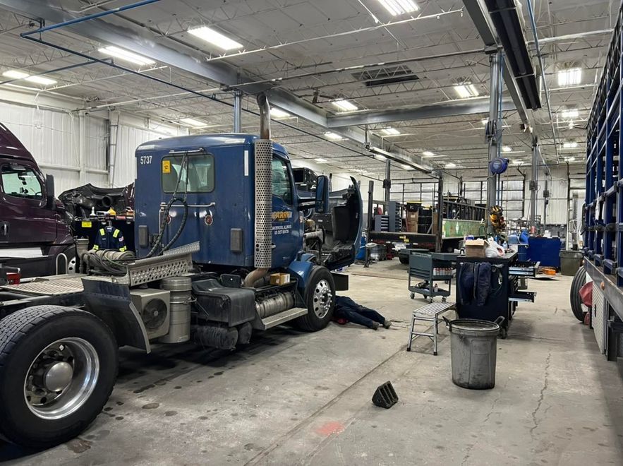 Truck repair shop with a blue semi-truck cab and mechanic equipment inside a bright garage