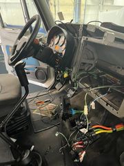 Damaged vehicle cabin with exposed wiring, steering wheel, and debris scattered on the floor