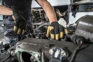 Mechanic wearing black-and-yellow gloves working on a car engine in a garage